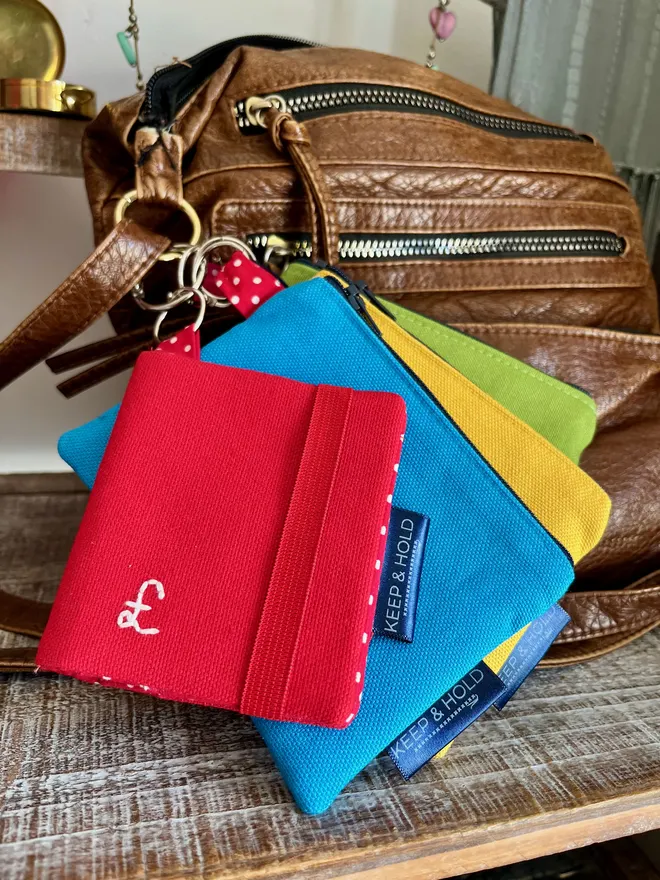 Set of colourful coin purses and a red card wallet attached to the d-ring on a handbag strap.