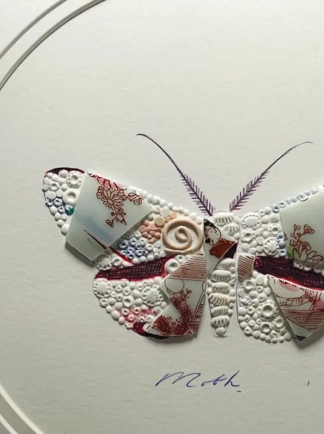 Hand-drawn, painted, mosaic clay, vintage pink floral Geisha pottery insect on white double mounted card, in a black circular frame.