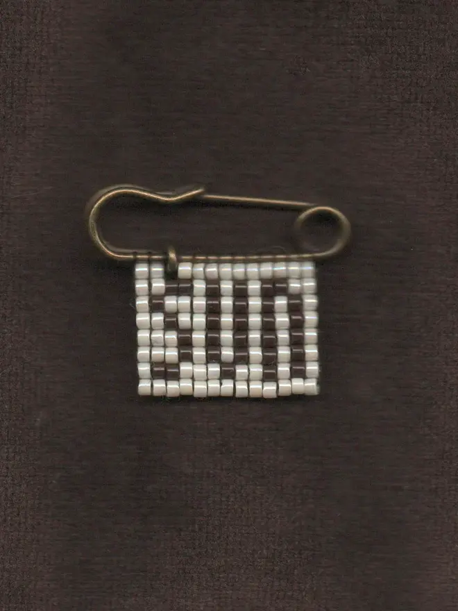 'linga IX' beaded 'sun' pin. a beaded pin badge with the word sun in brown lettering on a pearl background.