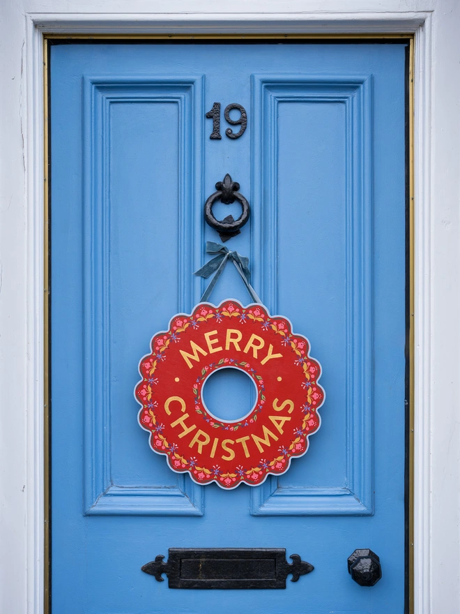 Red Hand painted Christmas Wreath with red lettering and gold leaf lettering on a blue front door