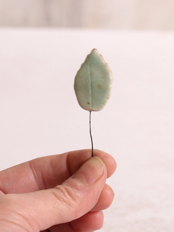 ceramic leaf held in a hand against a white background