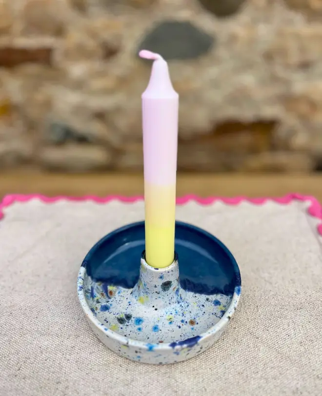 Shoreline Candle Stick Holder, a colourful candle stick holder sitting on a napkin, on a wooden surface against a brick backdrop. 