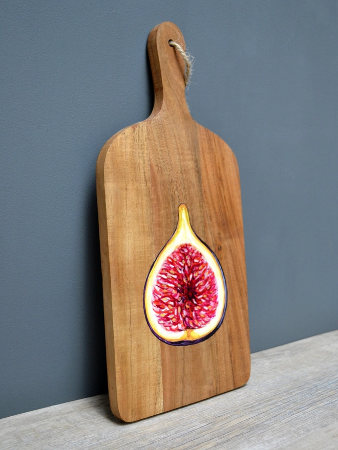 A wooden serving board with a handpainted design of a ripe fig