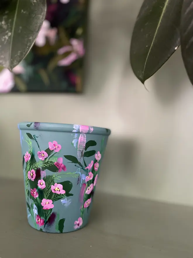 hand painted terracotta floral plant pot dark sage green background with vibrant pink wax flowers 