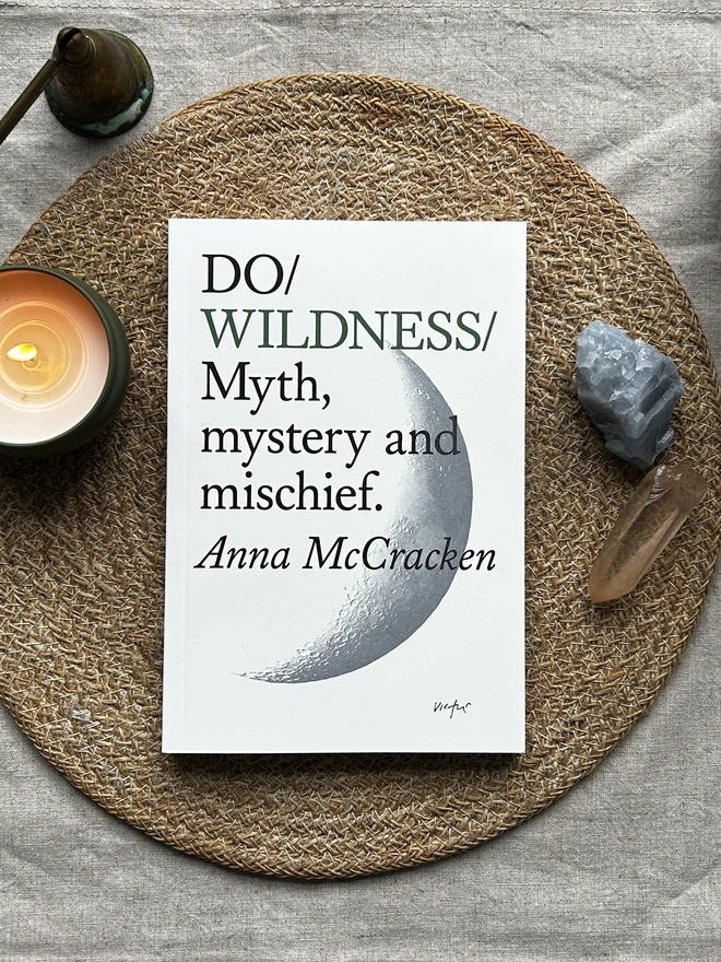 Paperback book on table surrounded by two crystals and a candle