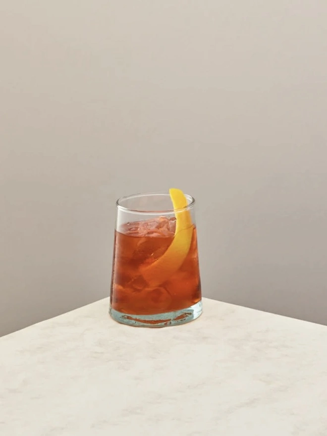 Tumbler Glasses (Set Of 1 Or 4), a tumbler glass sitting on a plain counter top against a plain backdrop. The glass contains a soft drink in it. 