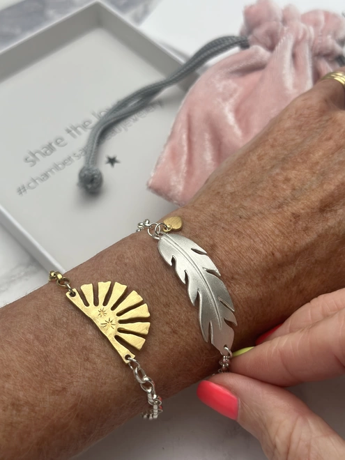 model wears a sterling silver feather charm on a silver belcher bracelet with mini heart charm in gold