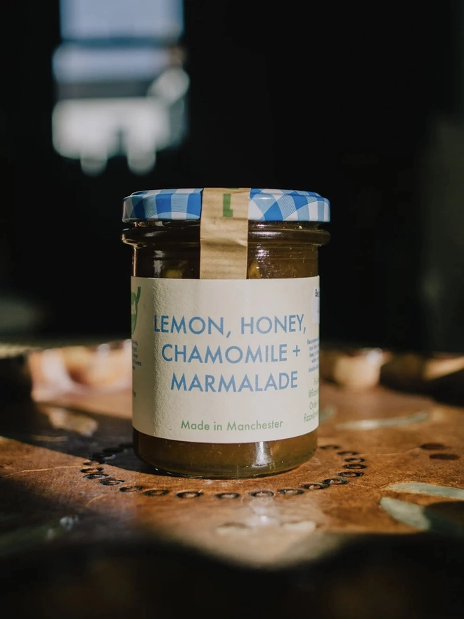 Lemon, Honey & Chamomile Marmalade Jar, jar of marmalade with a blue lid on a decorated plate on a table. 