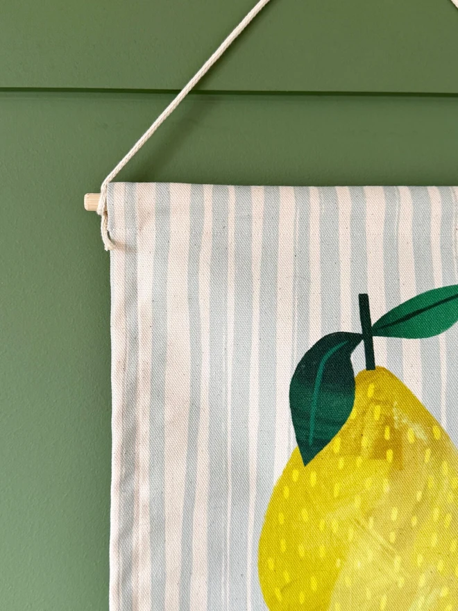 Cotton Lemon Wall Hanging, hanging on a green wall. 