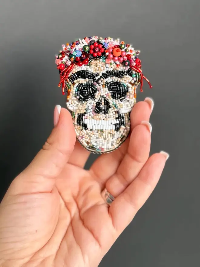 Frida Kahlo Skull Beaded Brooch, displayed in a hand, against a plain background. 