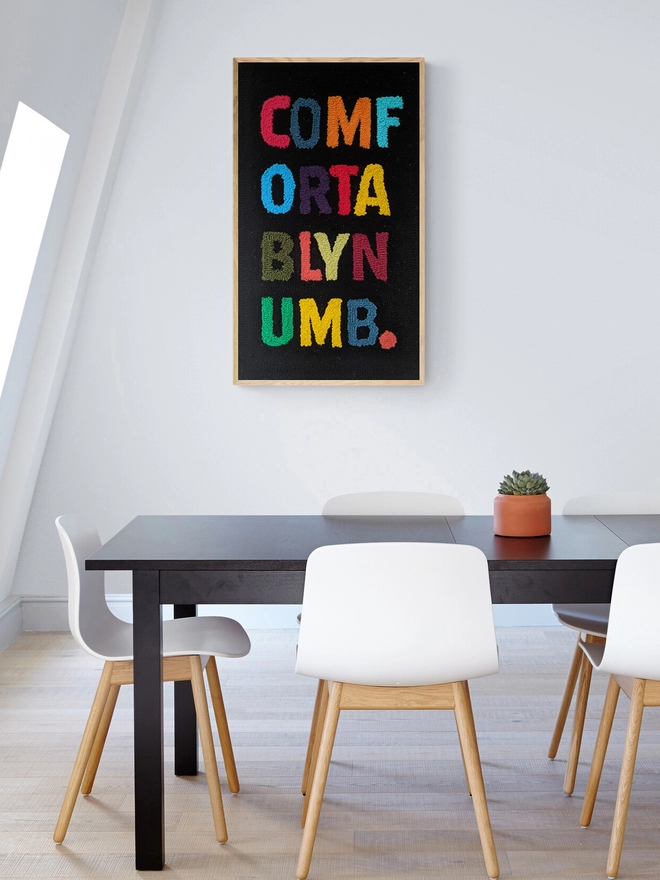 Comfortably Numb artwork in a wooden frame on the wall in a kitchen with table and white chairs