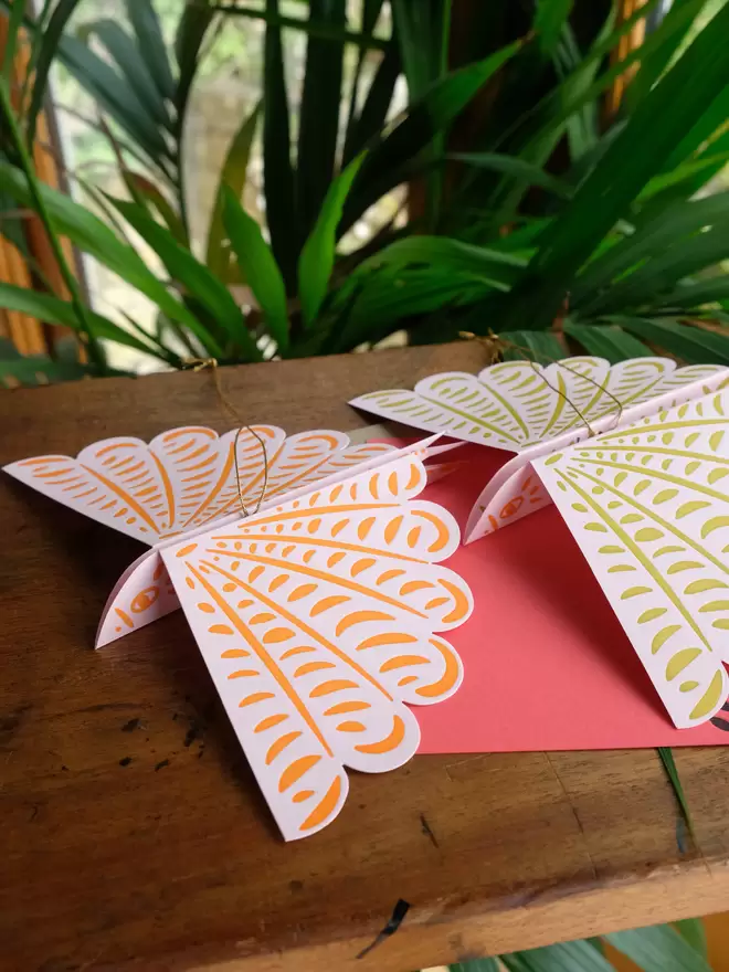Two bird decorations laying flat with wings out and message card underneath.