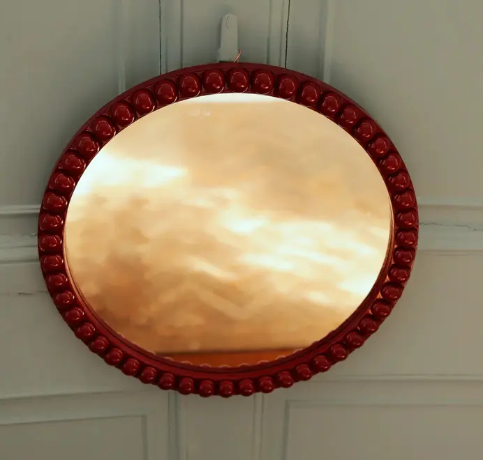 Round oversized bobbin mirrors in red hanging on a sage wall. 