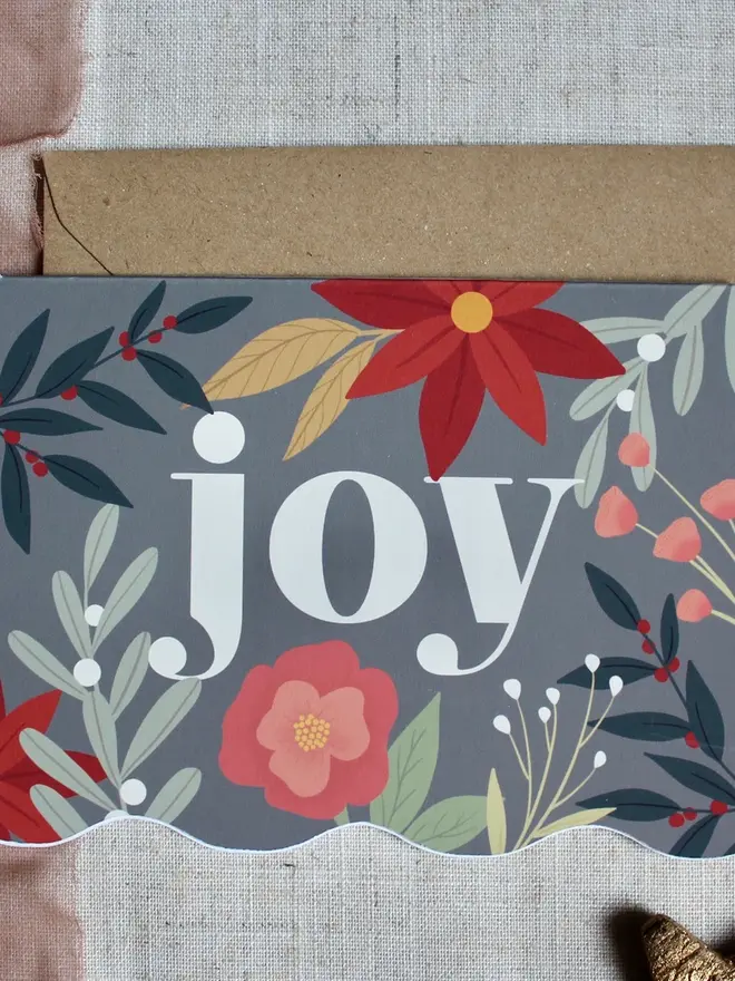 floral joy christmas card. wavy edged card decorated with the word joy and illustrated flowers.