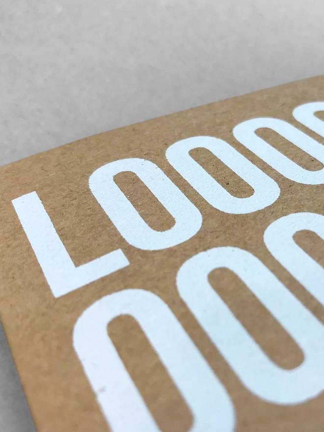 Close up of the white ink on kraft brown card, showing the crisp edge of the printed lettering, letters L-O-O-O O-O in shot.