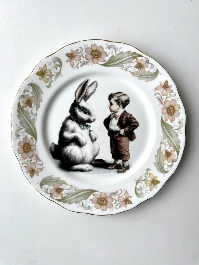 a vintage plate with decorative ornate borders, in the centre i have printed a vintage black and white illustration of a little boy talking to a giant pet white bunny rabbit