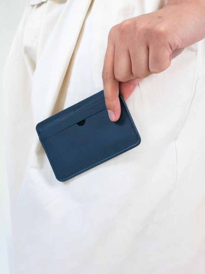 navy blue cardholder held between fingers in front of a cream coloured oversized trousers