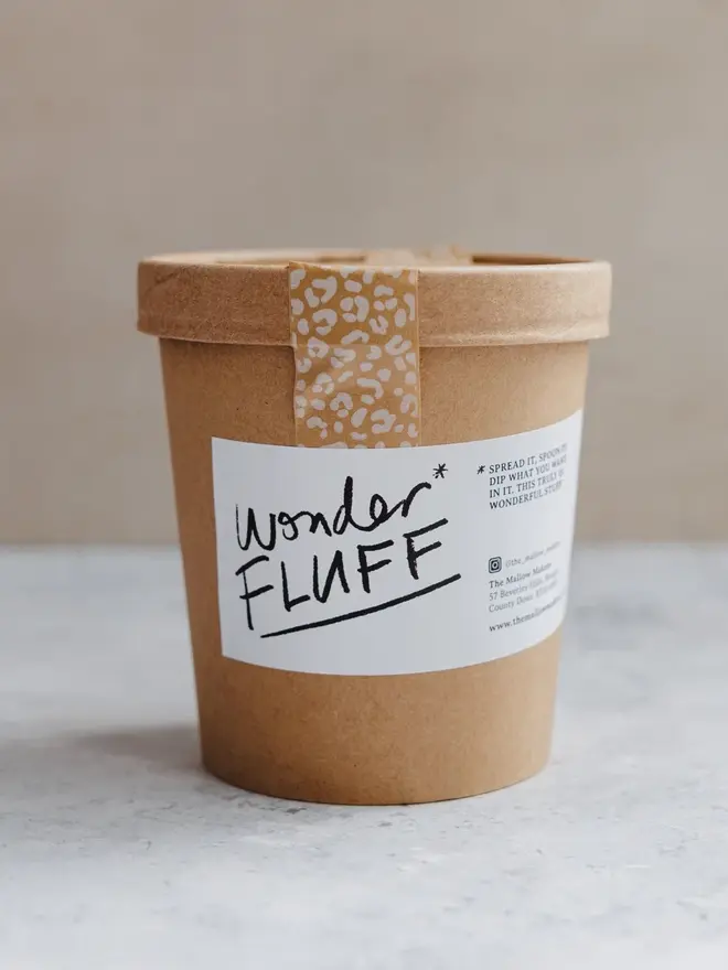 Vanilla Wonder Fluff Tub, the tub on a white surface. This is in front of a brown background. 