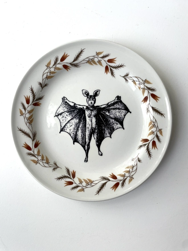 vintage plate with an ornate border, with a printed vintage illustration of a bat boy in the middle 