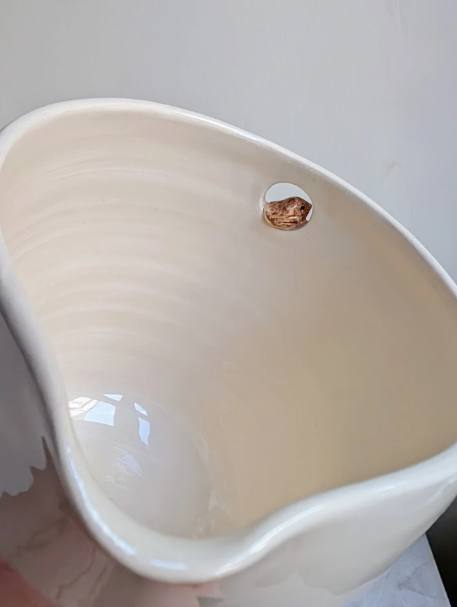 close up of a handmade ceramic white jug with a tiny robin bird in a small cut out hole