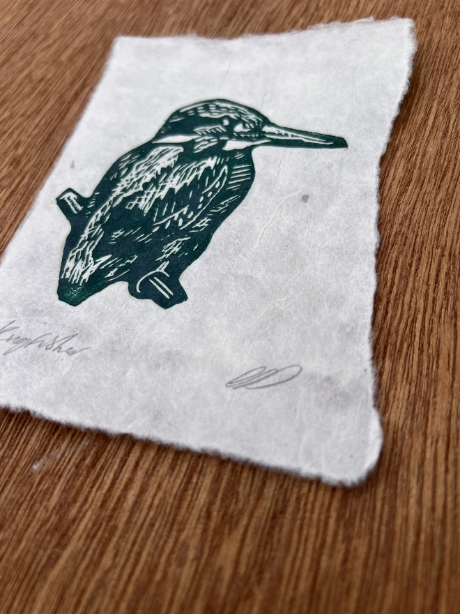 Close-up of a hand-printed green kingfisher lino print showing the carved detail, ink texture and natural grain of the handmade paper.  