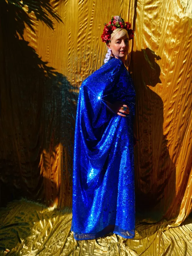 Fumbalina Royal Blue Holographic Sequin V-neck Kaftan Gown seen from the side with hands on hips.