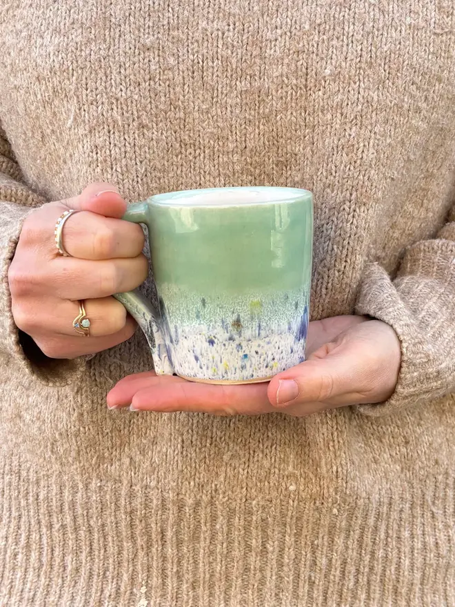 Shoreline Standard Mug, a colourful mug held in front of a person in a jumper. 