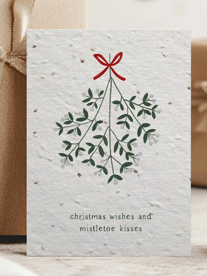 Christmas Card with illustration of mistletoe with 'Christmas Wishes and Mistletoe Kisses'. In the background is Christmas presents.