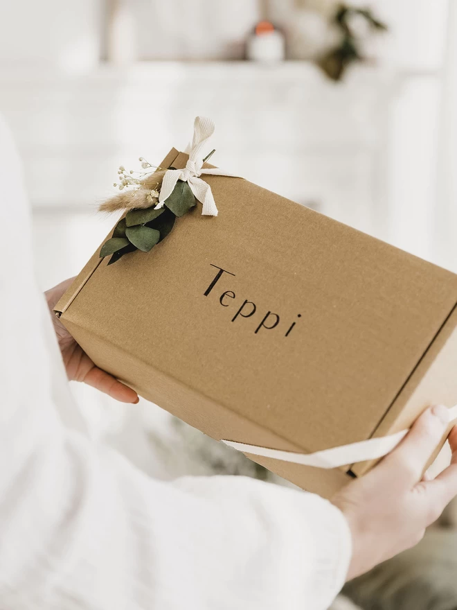 hands holding a brown box, tied with cream ribbon and a selection of dried flowers