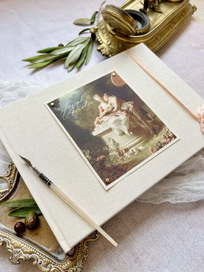 Luxury fabric printed wedding guest book featuring an images of lovers from an 18th century rococo work of art. Linen covered book finished with ribbon