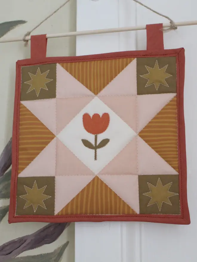 tulip quilt wall hanging. a patchwork quilt with a pink star pattern in the centre and embroidered tulip.