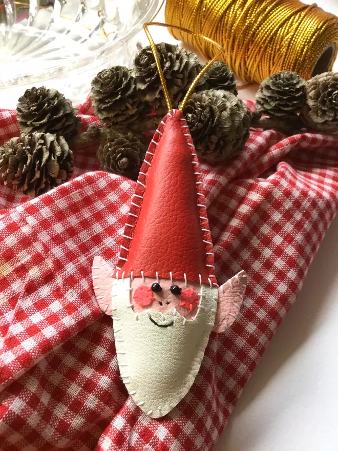 A hand stitched faux leather Christmas elf tree decoration on red gingham fabric background