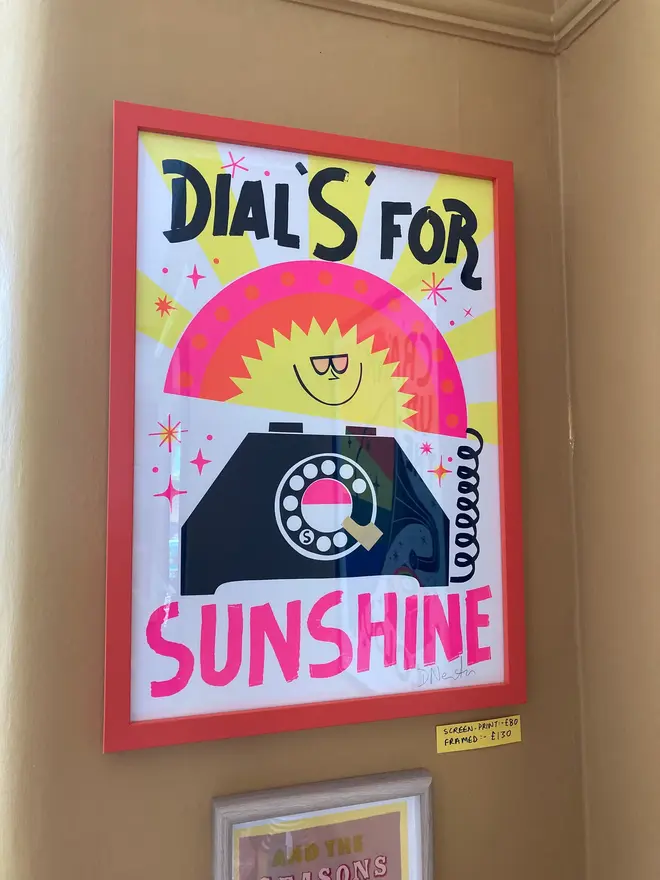 'Dial S For Sunshine' Screenprint, a colourful screenprint sitting in a pink frame on a plain backdrop. The screenprint reads 'Dial s for sunshine'. 