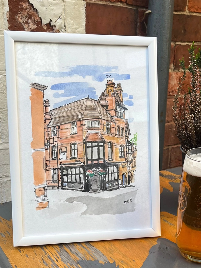 watercolour painting of a Pub, in white frame, leaning against a wall
