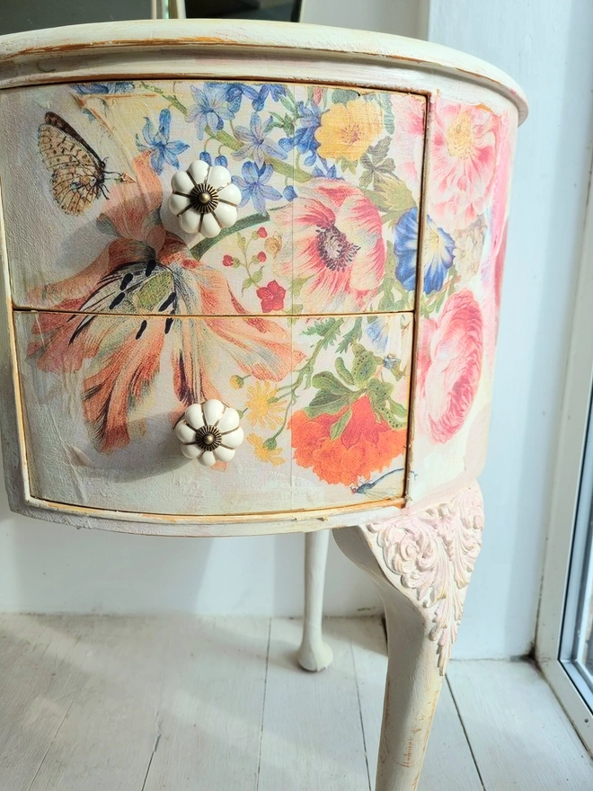 An antique kidney-shaped dressing table with chair and a trio of mirrors. Upcycled in cream and pale pink with decoupage florals in oranges and pinks. Text across the table read ‘flowers make me happy’ in the orange of the undercoat.