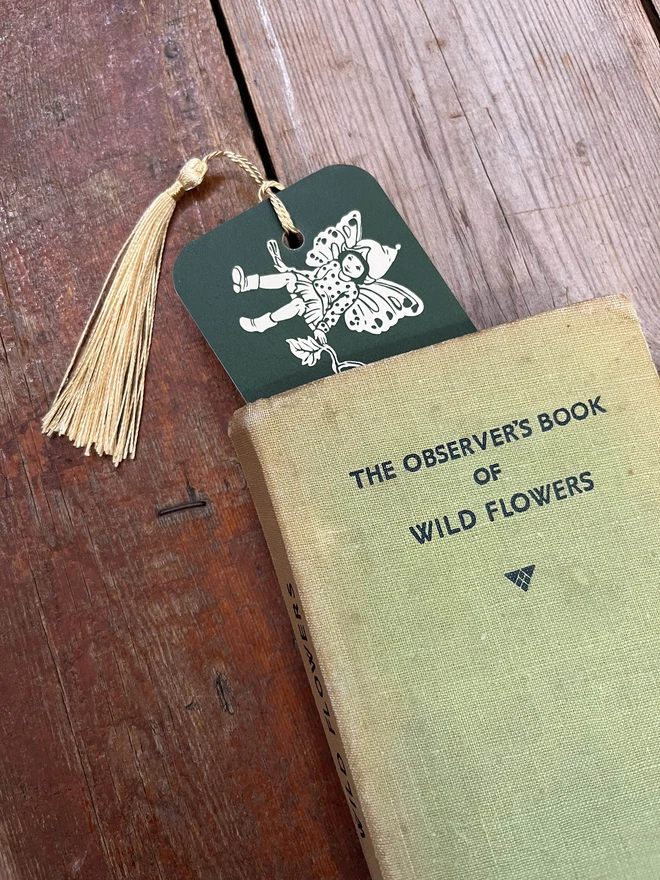 a close up of the end of a boomark a pixie peeking out of a vintage book drawn in a traditional vintage style bottle green in colour with a pale golden pixie