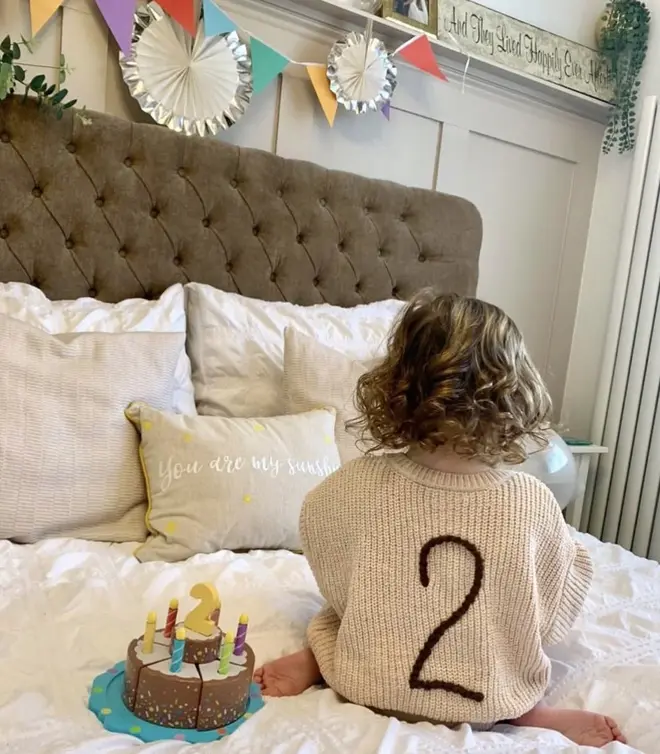 Birthday Cardigans, a baby with a personalised birthday cardigan sitting on a bed decorated by birthday items. 