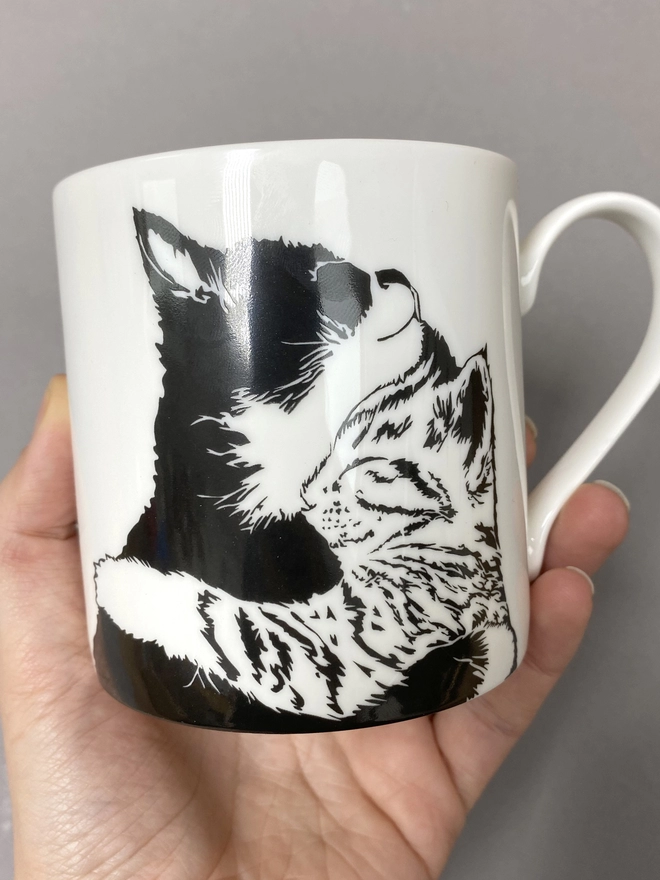 Close up of the 'Cuddle Time' mug showing a black and white and tabby cat lovingly cuddling each other