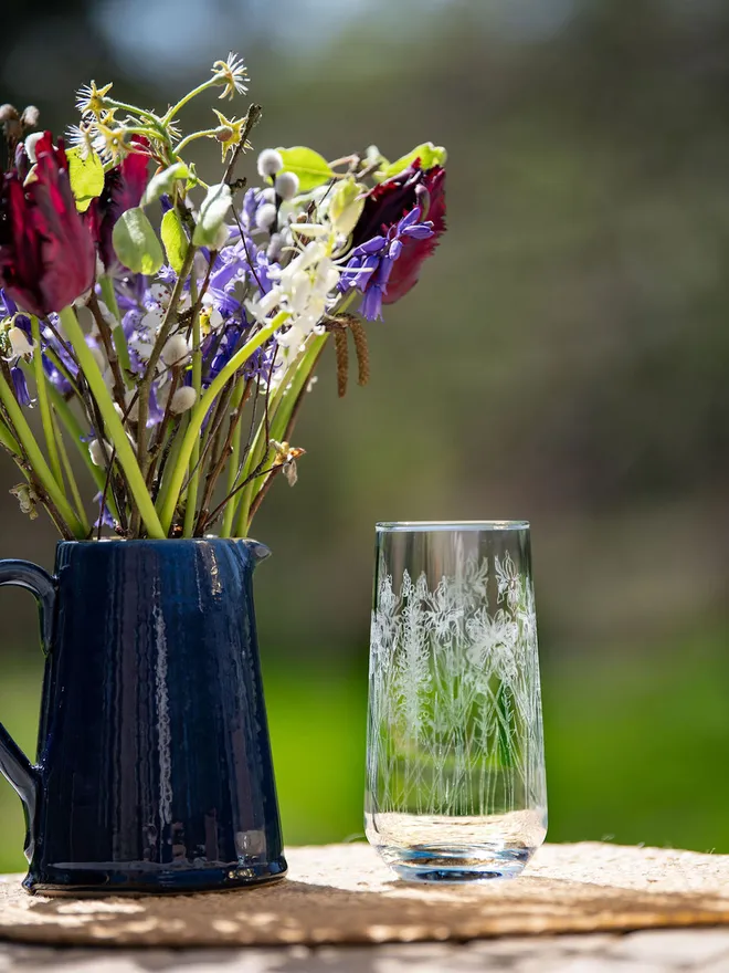 A set of tall, floral-etched highball glasses on an outdoor table.