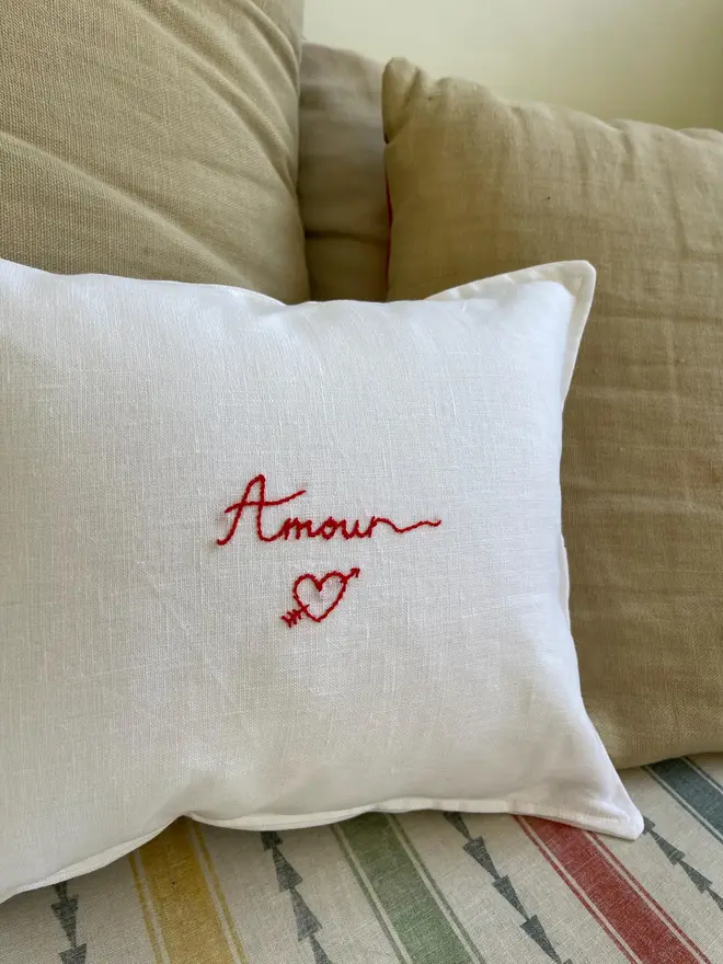 'Amour' Hand Embroidered Linen Cushion Hearth Design, white cushion on a sofa. 