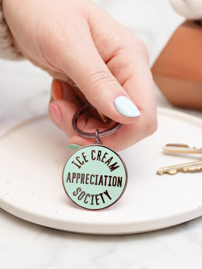 Hand holding a Mint green enamel keyring with 'Ice Cream Appreciation Society' design