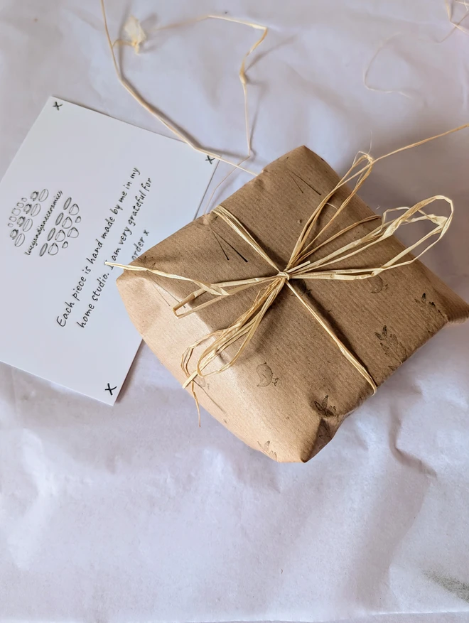 gift wrapped parcel in brown hand printed paper and natural raffia on a white paper background with a postcard thank you note