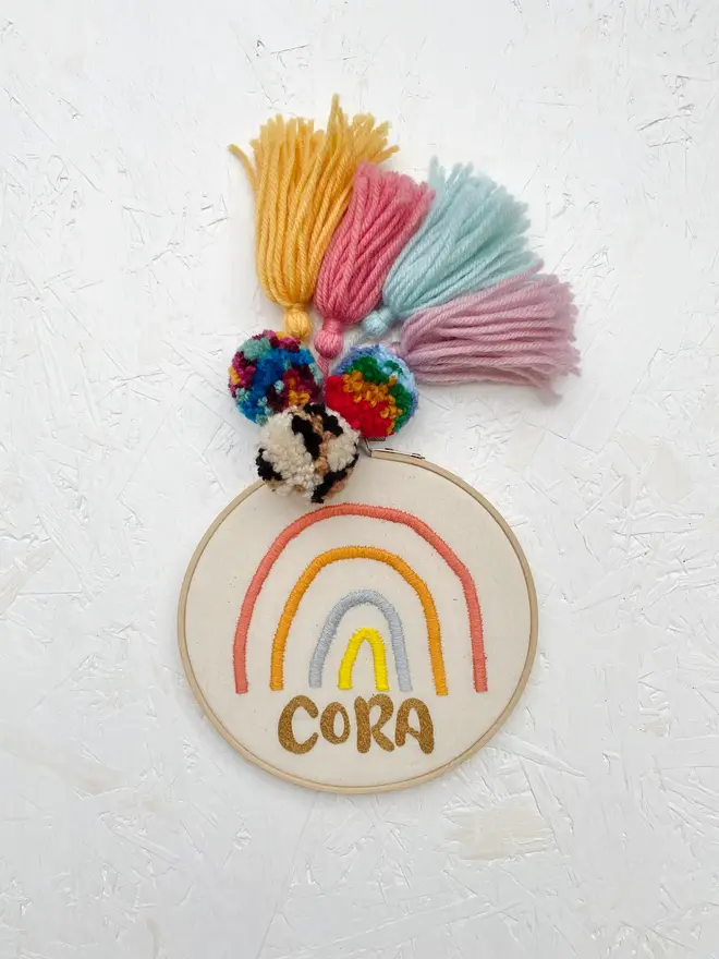personalised name and rainbow embroidered hoop. cotton hoop embroidered with the name michaella and a red, yellow and blue rainbow.