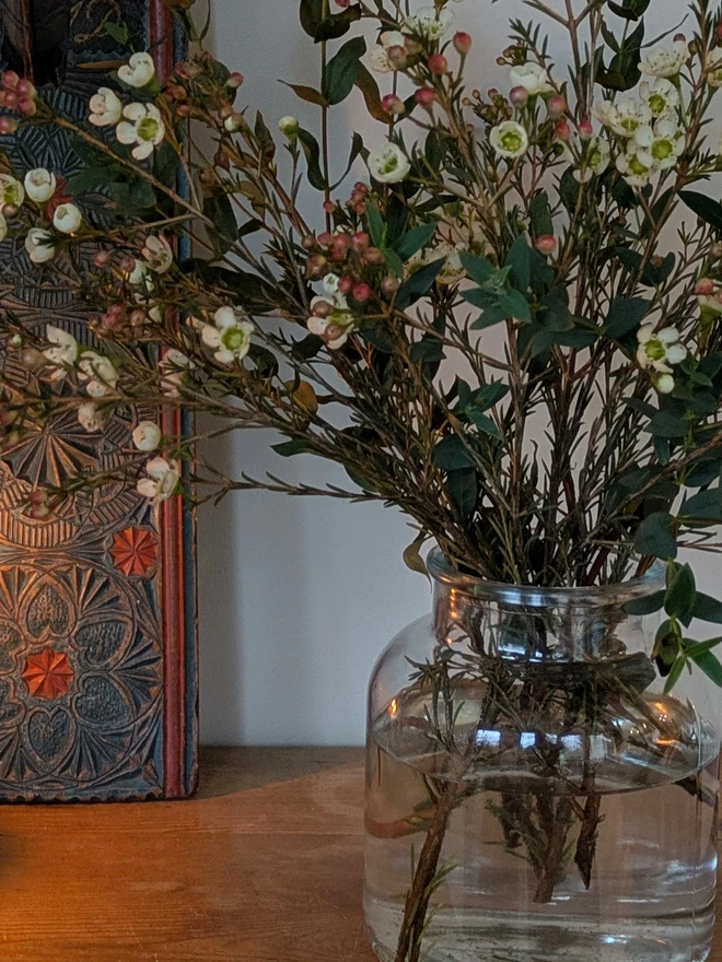 Fresh White Wax Flowers mixed with blue eucalyptus stems in a clear vase on wooden surface