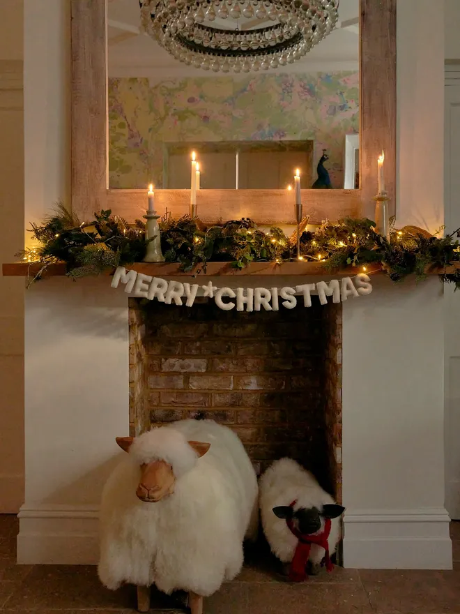 A white Merry Christmas garland, hung on a mantelpiece.
