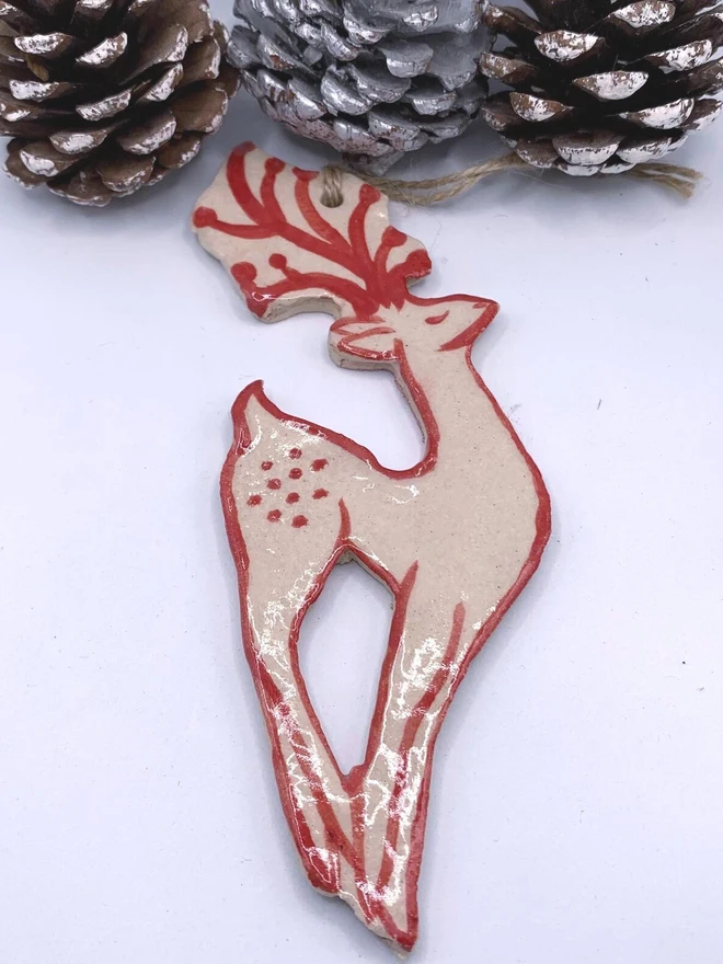 Handmade Ceramic Reindeer Ornament Scandinavian Folk Decor, a colourful reindeer decoration sitting on a plain surface joined by some acorns. 