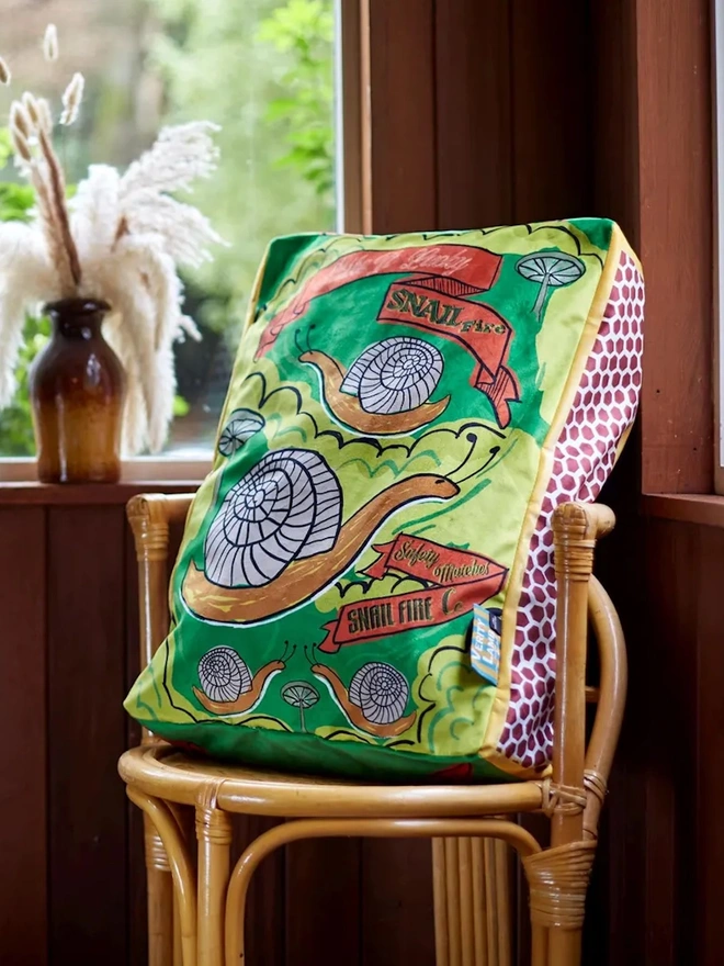 Snail Matchbox Cushion, a green decorated cushion sitting on a chair. 