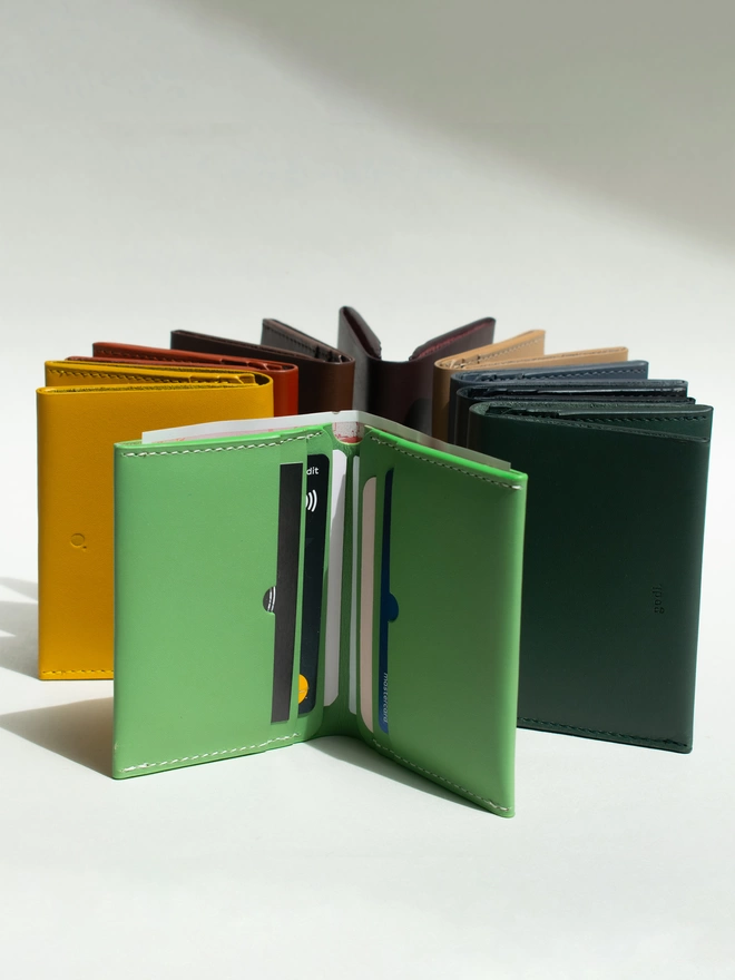Bifold Wallets standing in a circle formation with a sea green facing the front open. The sea green wallet is filled with cards and a £50 note