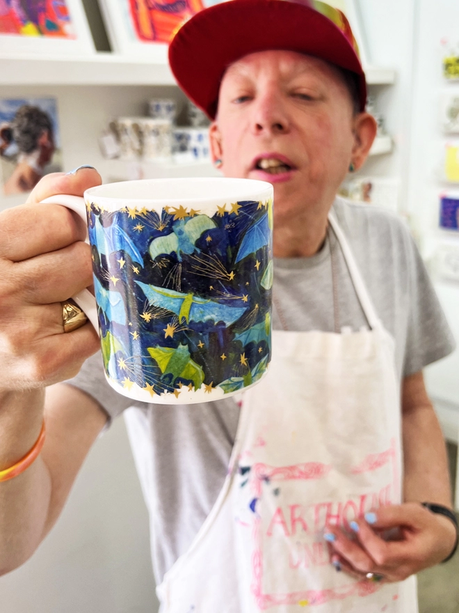 Happy  artist holding bats fine bone china charity gift mug featuring gold, green & blue illustrations