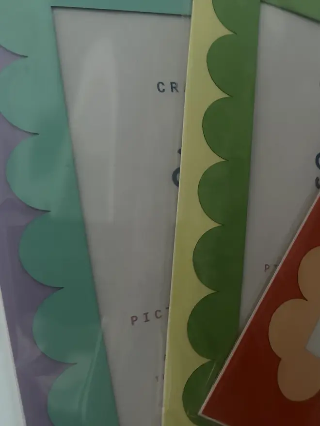 Scallop Edged A5 / A4 photo mount. close up of purple, yellow and red variants held against grey background.